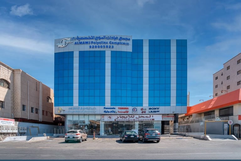Modern blue glass commercial building with ground-level storefronts and parked cars on a sunny day